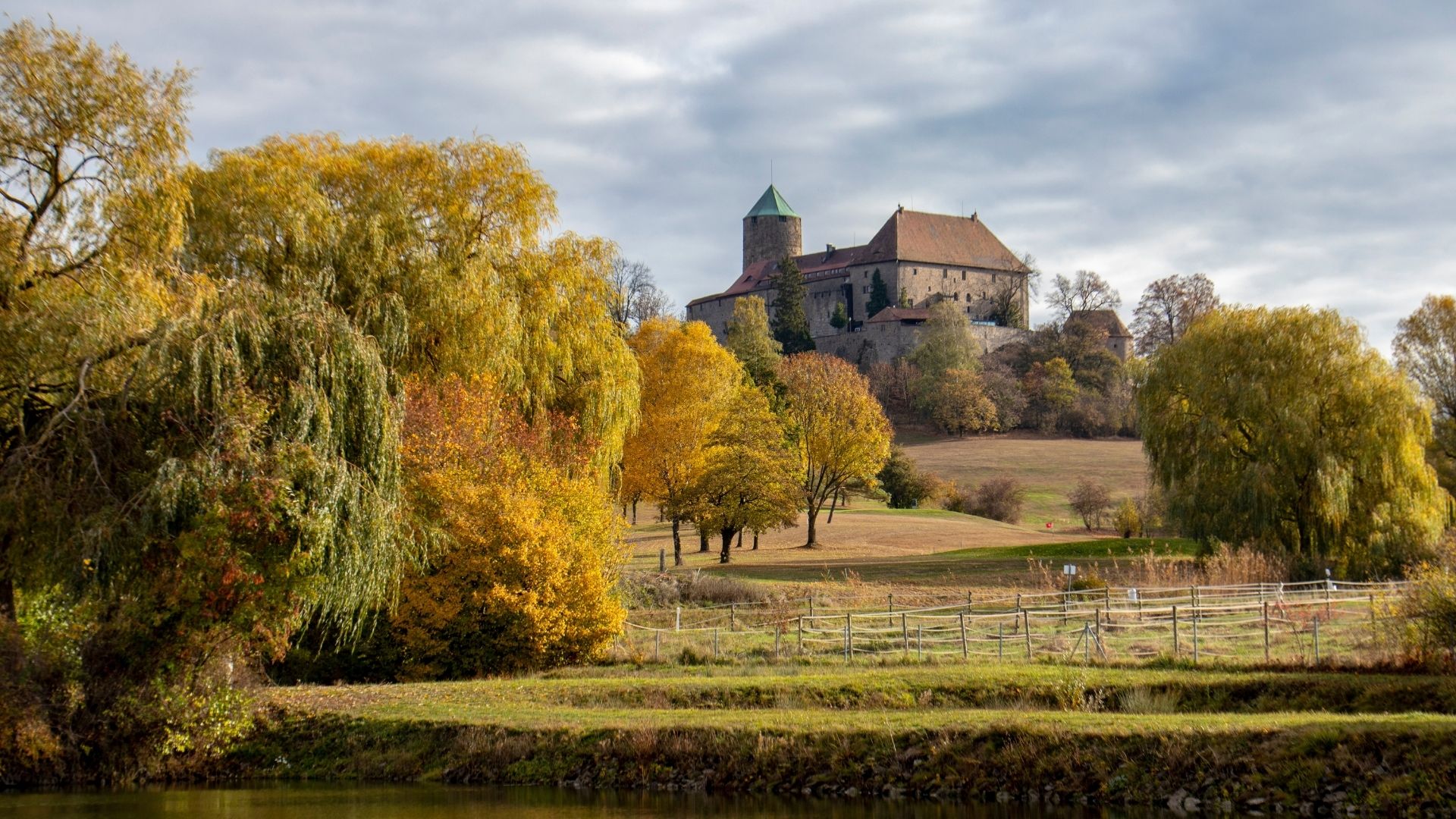 Burg Colmberg auf einem Hügel umgeben von herbstlich gefärbten Bäumen und einer Wiese im Vordergrund