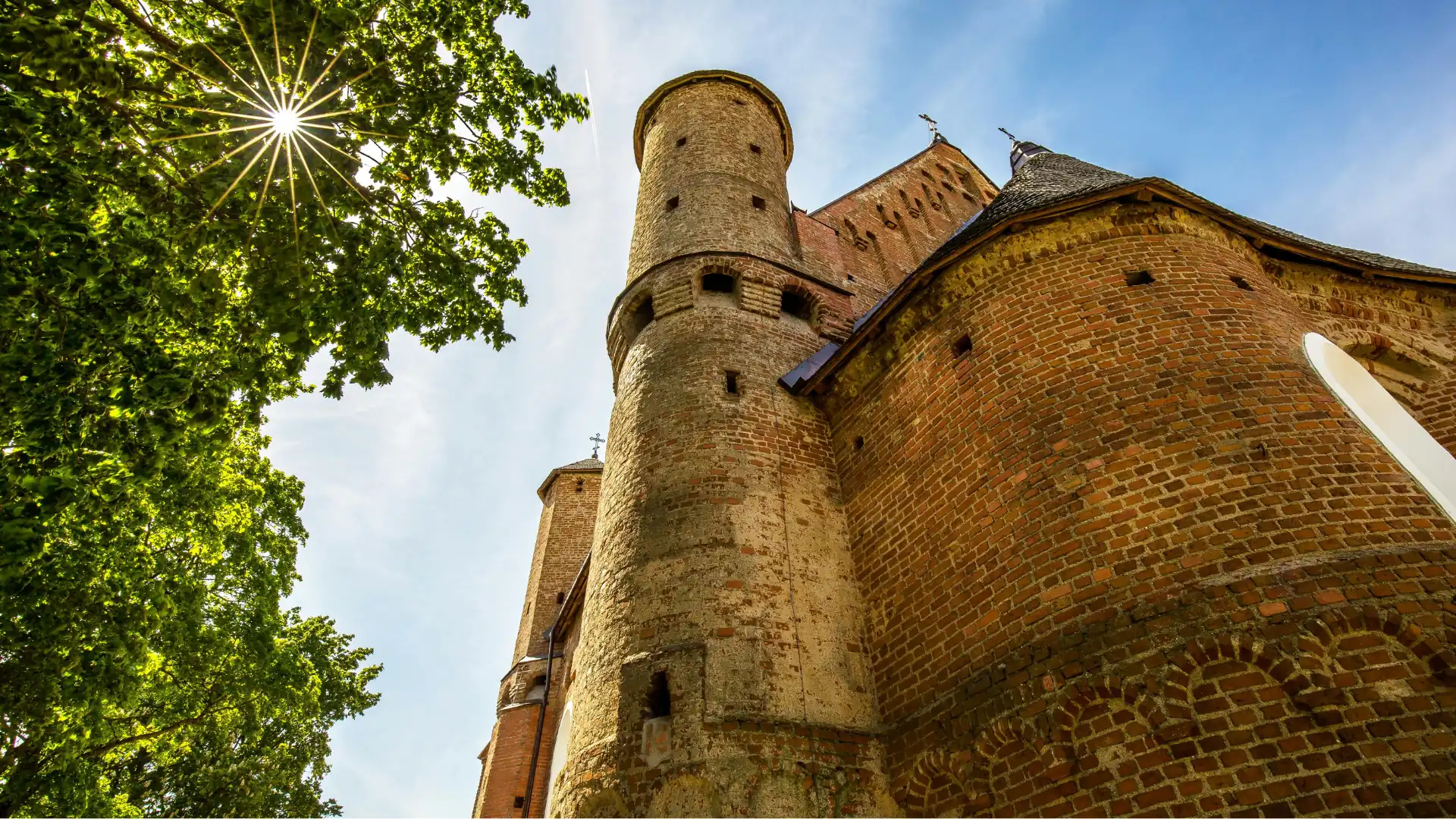 Blick nach oben auf einen runden, historischen Backsteinturm einer Burg in Cardiff mit grünem Laub und Sonne am Himmel