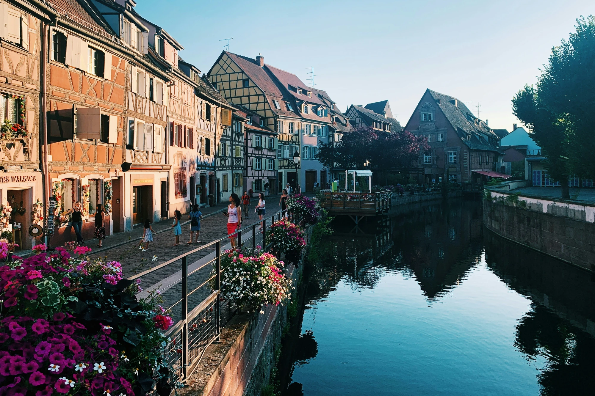 EGemütliche Altstadt von Colmar im Elsass, mit Blick auf den Fluss zur Zeit des Sonnenuntergangs. Die warmen Farben des Himmels spiegeln sich im Wasser, während die charmanten Fachwerkhäuser entlang des Ufers eine malerische Atmosphäre schaffen.