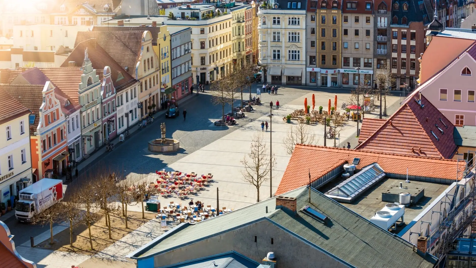 Luftaufnahme eines Platzes in Cottbus mit mehreren Gebäuden in verschiedenen Farben, Bäumen und Menschen, die sich im Freien aufhalten.