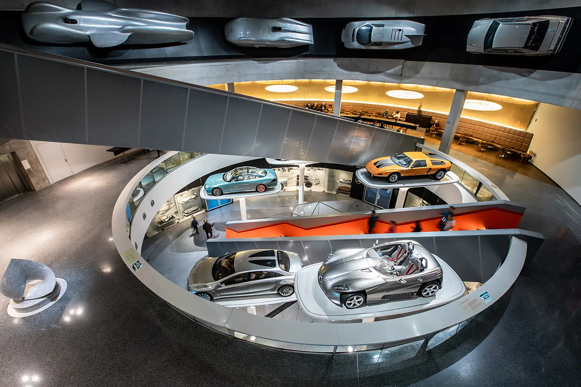 Ausgestellte Autos im Mercedes Benz Museum in der Mitte neben einer Treppe mit Menschen