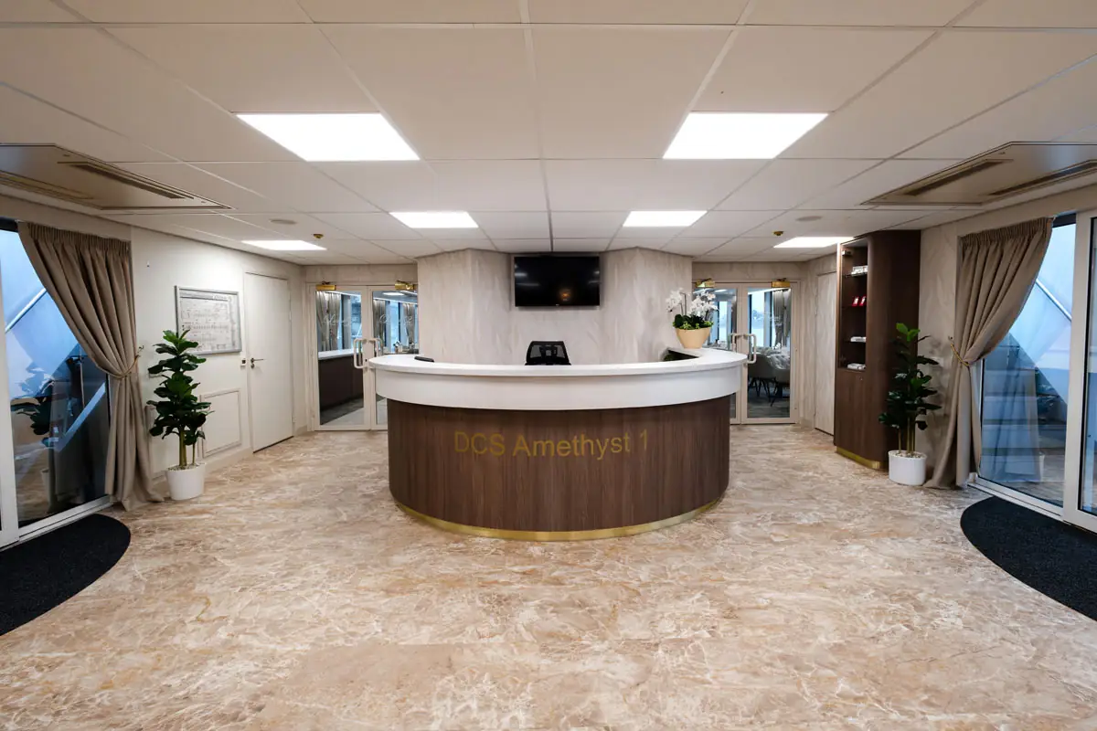 Runde Rezeption mit Schriftzug 'DCS Amethyst 1' in einem modernen Raum mit großen Fenstern, Pflanzen und Vorhängen