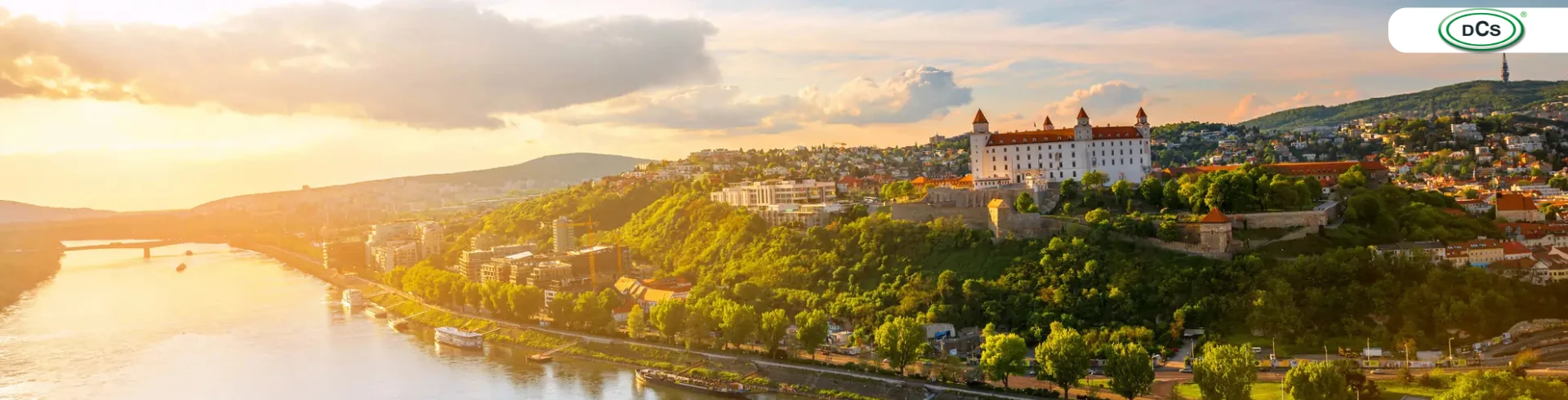 Fluss mit einem Frachtschiff und einer Burg auf einem bewaldeten Hügel bei Sonnenuntergang mit DCS Logo in der Ecke