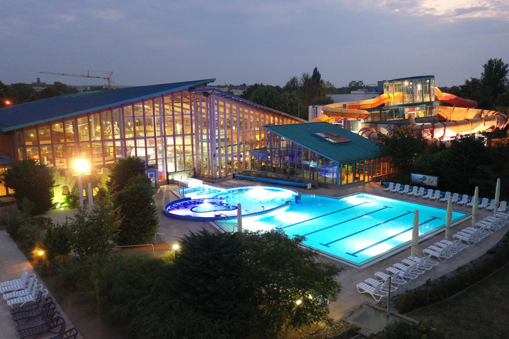 Das Wonnemar Resort in Wismar beeindruckt mit einer beleuchteten Außenansicht bei Abenddämmerung, die das großzügige Schwimmbad, die Rutschenlandschaft und die modernen Glasfassaden in Szene setzt.