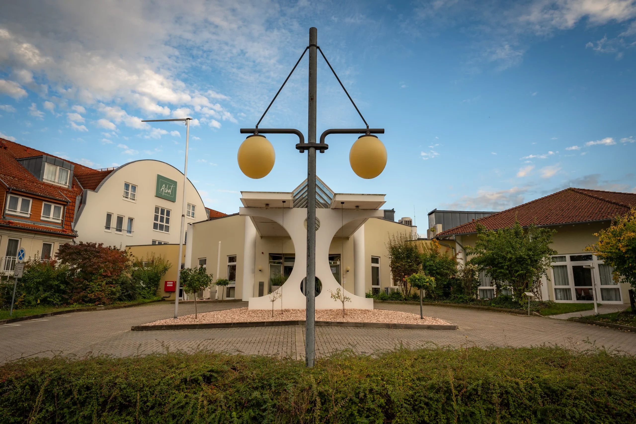 Vordergrund mit einer Laterne mit zwei runden Lampen vor dem Eingangsbereich eines Hotels mit weißer Fassade und roten Dächern