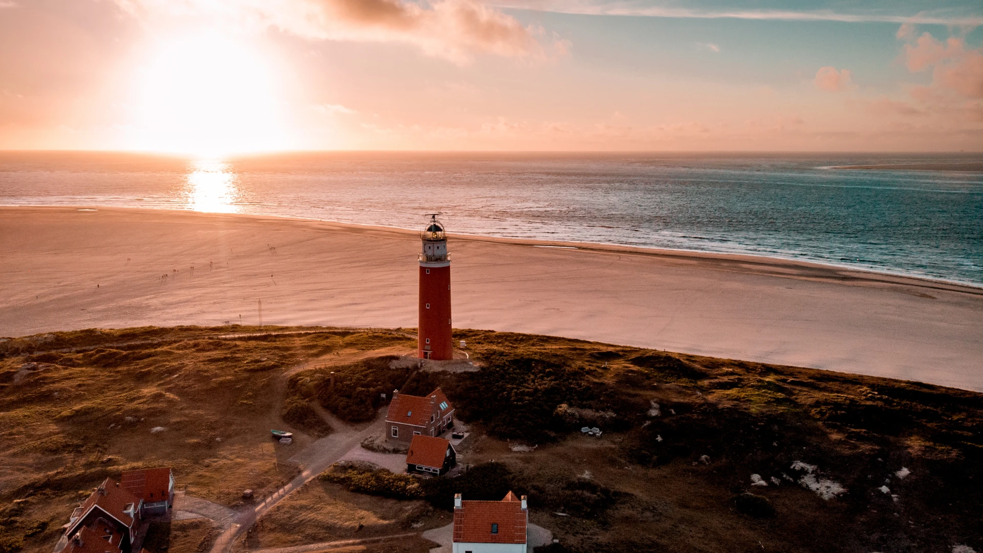 Roter Leuchtturm am Strand der Insel Texel mit Sonnenuntergang am Meereshorizont