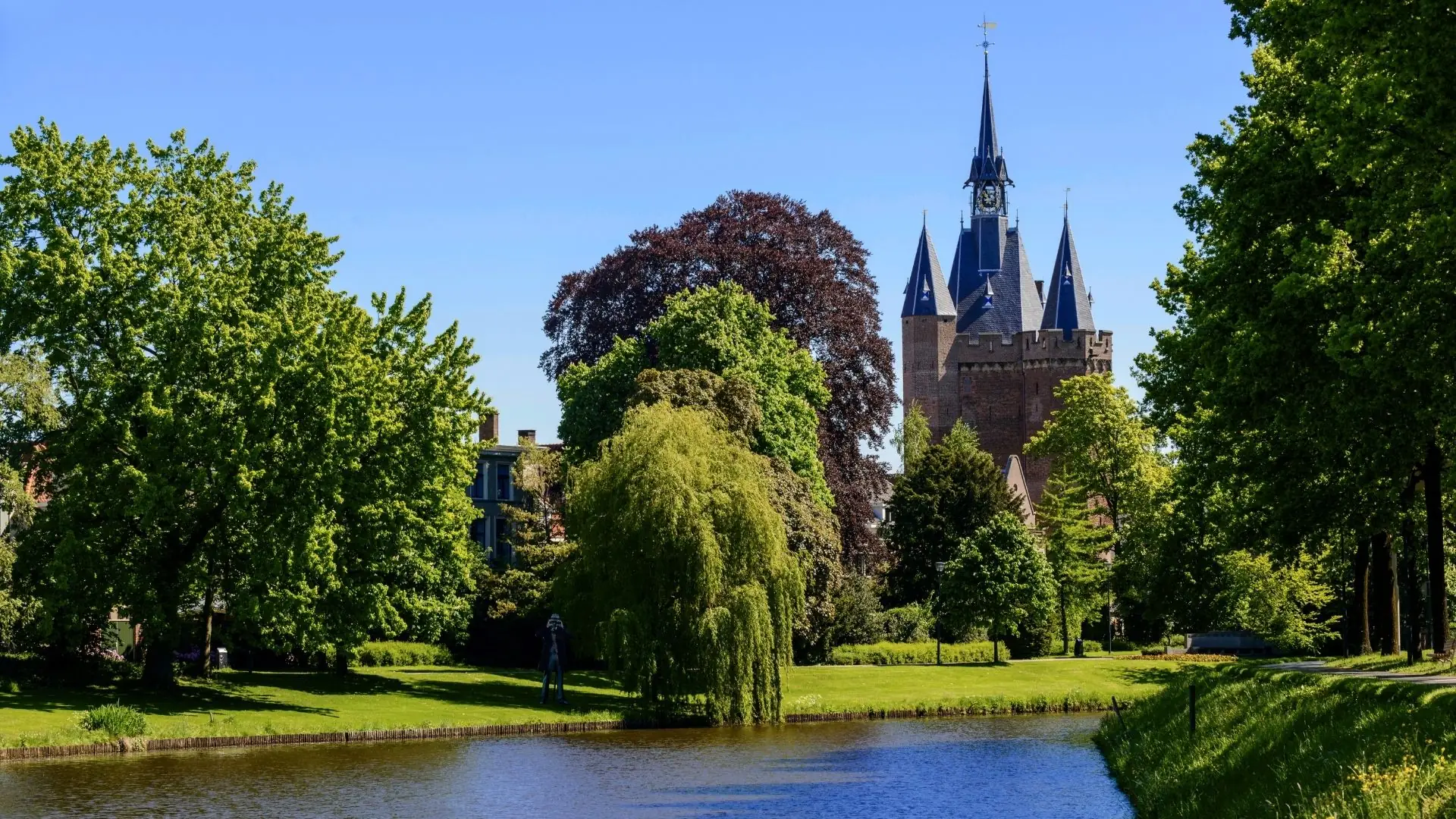 Das Sassenpoort in Zwolle mit spitzen Türmen, umgeben von grünen Bäumen und einem Wassergraben im Vordergrund.