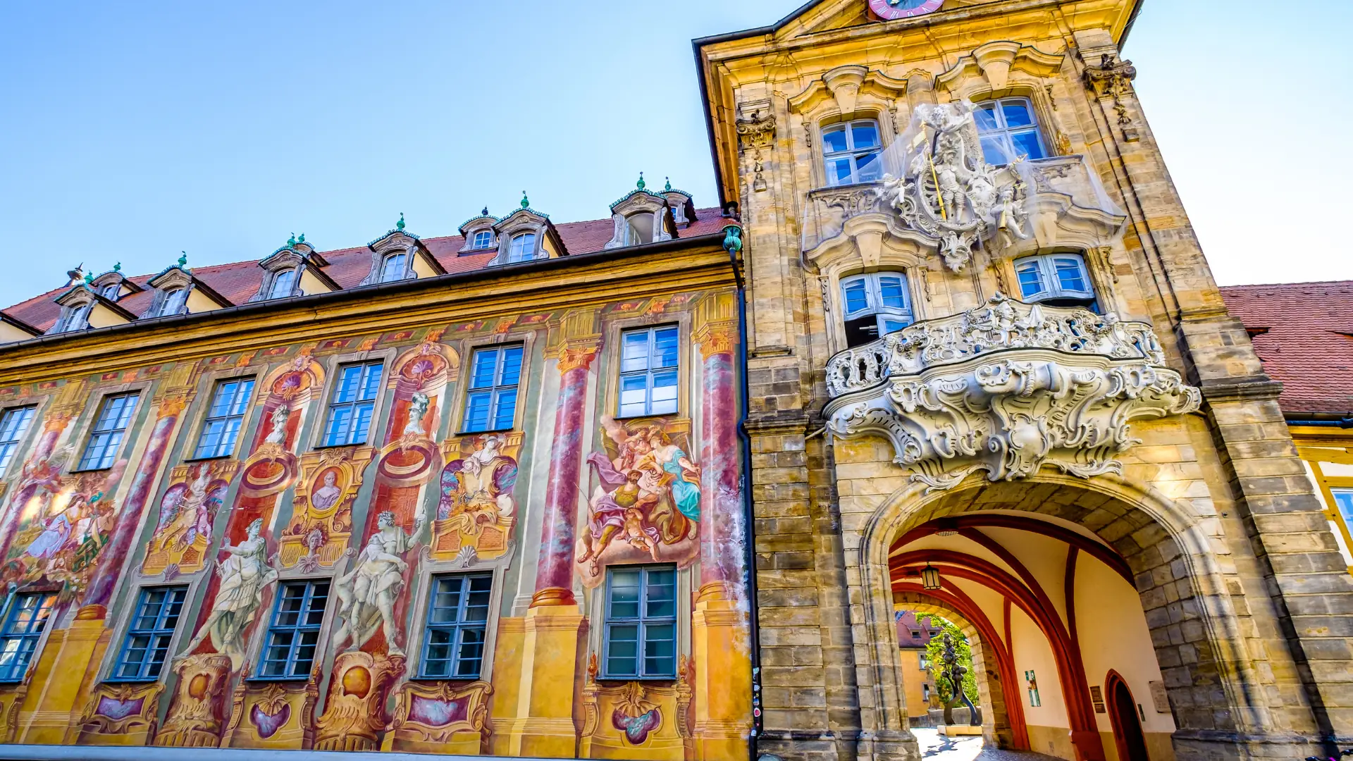 Das Bild zeigt das Alte Rathaus in Bamberg mit bunten Malereien im Barock und Rokokostil. Die Fassade ist mit vielen Verzierungen und verspielten Formen geschmückt.