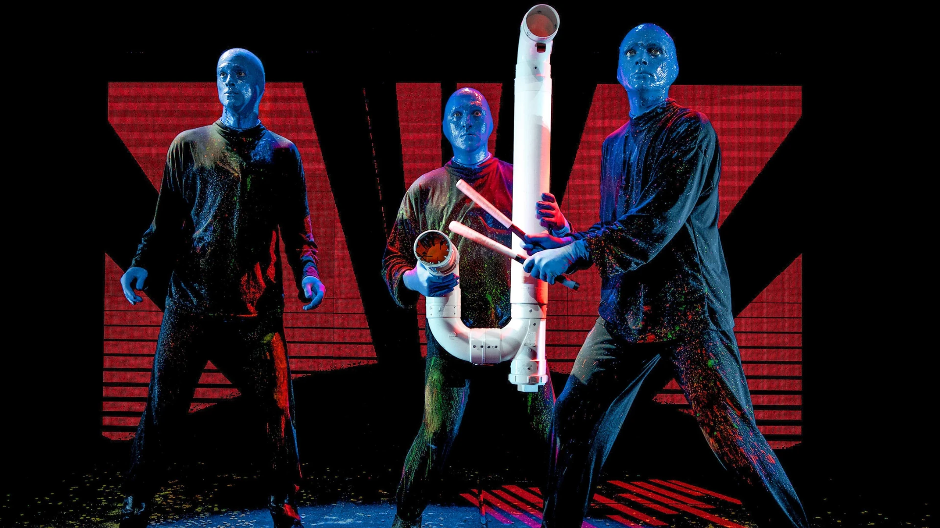 BLUE MAN GROUP Show in Berlin - Szenenmotiv - 3 blaue Männer in schwarzer Kleidung mit Drum Sticks und Rohren