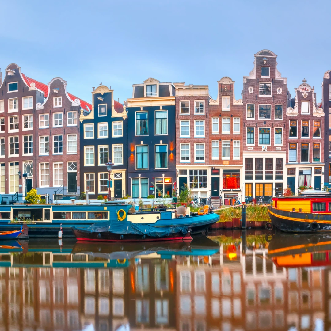 Dieses Foto zeigt eine typische Amsterdamer Gracht mit malerischen, schmalen Giebelhäusern und Hausbooten, die sich im ruhigen Wasser spiegeln. Die bunten Fassaden und die historische Architektur verleihen der Szene einen charmanten und authentischen Charakter.