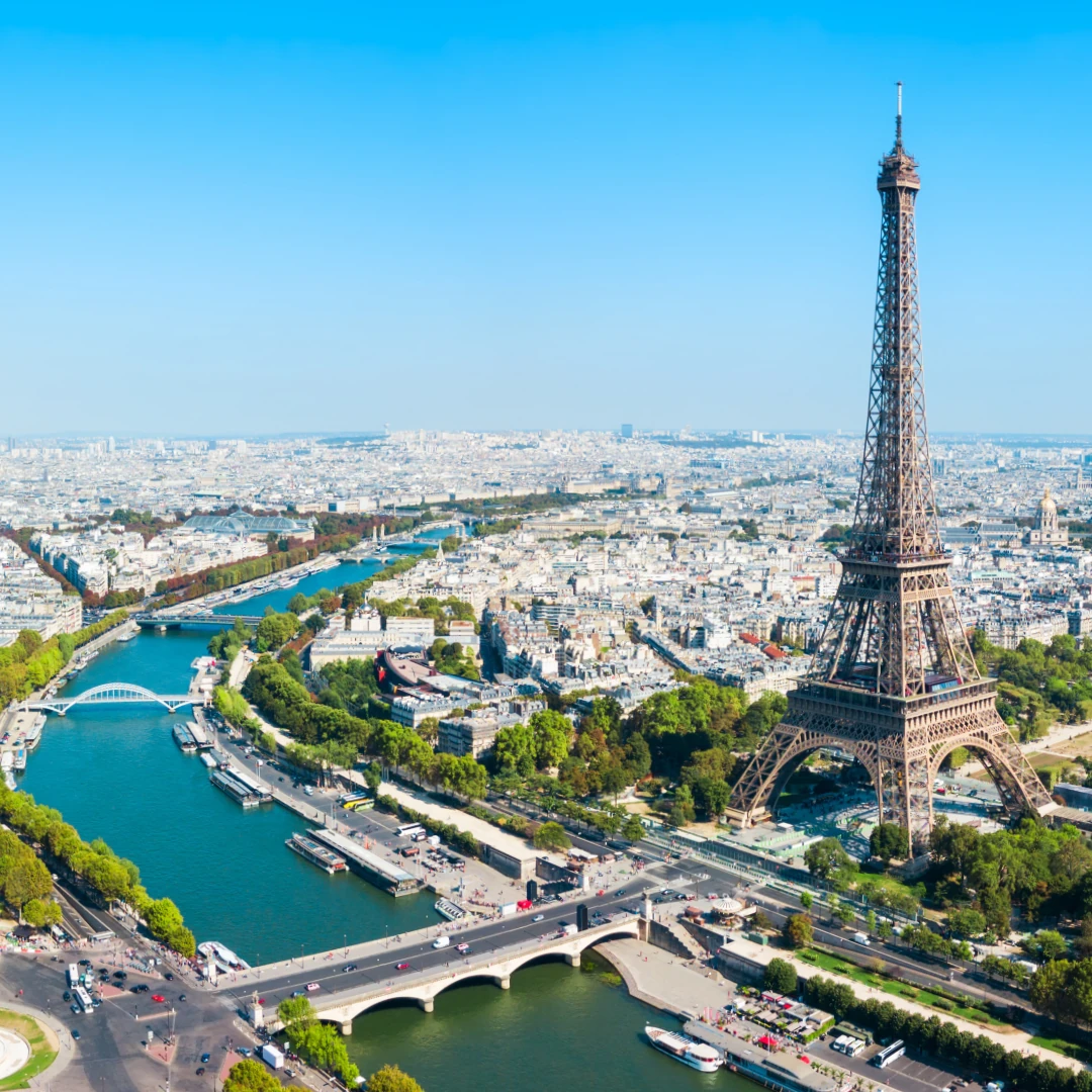 Dieses Foto zeigt eine beeindruckende Luftaufnahme von Paris mit dem Eiffelturm als zentralem Blickfang. Die Seine schlängelt sich durch die Stadt, umgeben von historischen Gebäuden und grünen Parkanlagen, die das typische Pariser Stadtbild prägen.