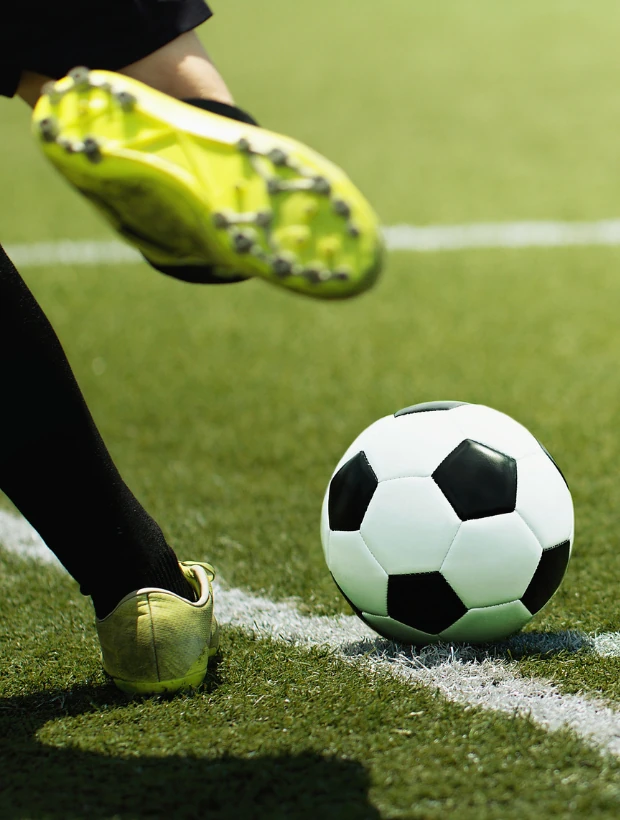 Fußballspieler mit gelben Schuhen kurz vor dem Schuss auf einen schwarz-weißen Fußball auf dem Spielfeld