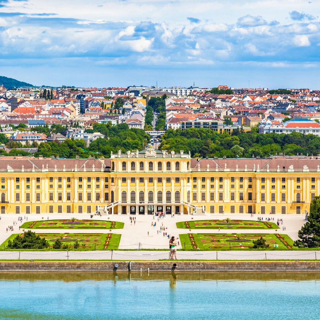 Dieses Foto zeigt das prachtvolle Schloss Schönbrunn in Wien, umgeben von seinen weitläufigen Gärten. Die barocke Architektur des Schlosses bildet einen eleganten Kontrast zur Skyline der Stadt im Hintergrund und spiegelt Wiens imperiale Geschichte wider.