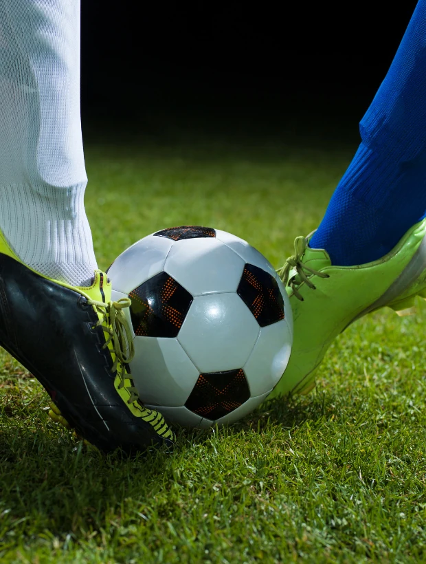 Fußballspieler mit schwarzen Stutzen und gelb-schwarzen Schuhen beim Schuss auf einen schwarz-weißen Fußball auf grünem Rasen