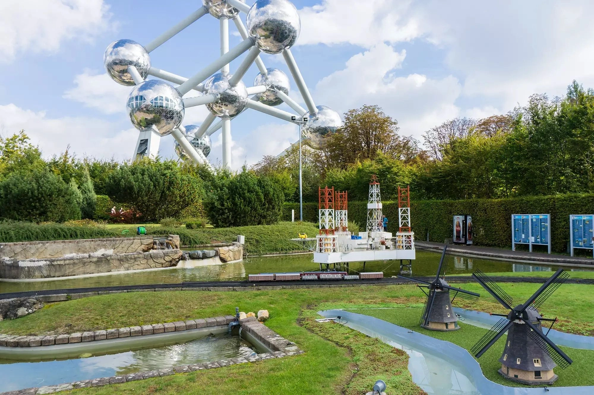 Themenpark Mini-Europa in Brüssel mit dem Atomium im Hintergrund bei Tageslicht, das die Miniaturmodelle europäischer Sehenswürdigkeiten umrahmt.