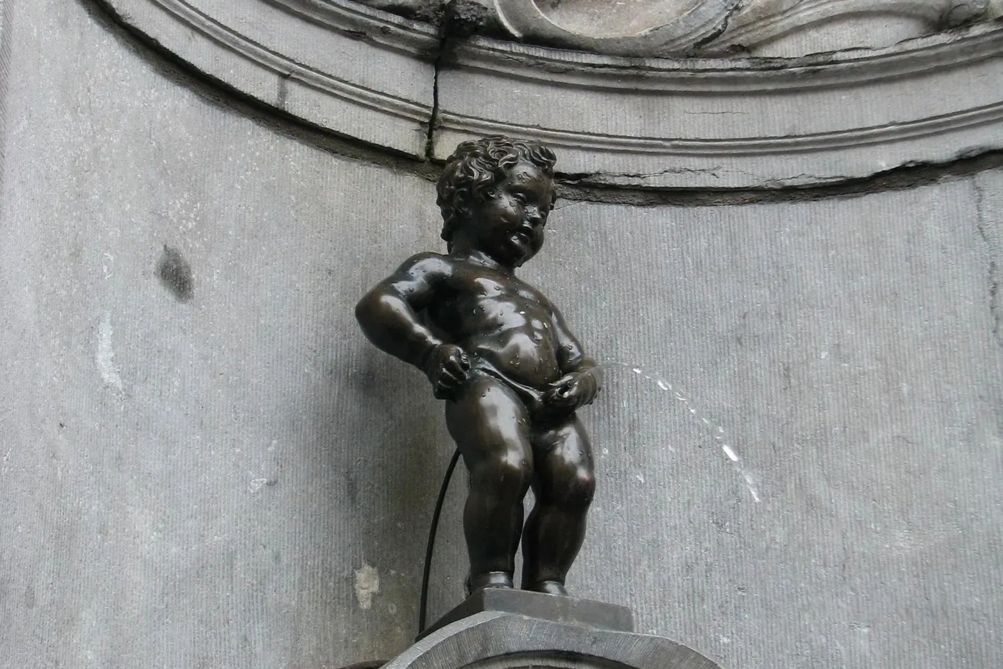 Die berühmte Bronzestatue Manneken Pis in Brüssel, die einen kleinen Jungen darstellt, der in einen Brunnen uriniert. Die Statue ist ein beliebtes Wahrzeichen der Stadt.
