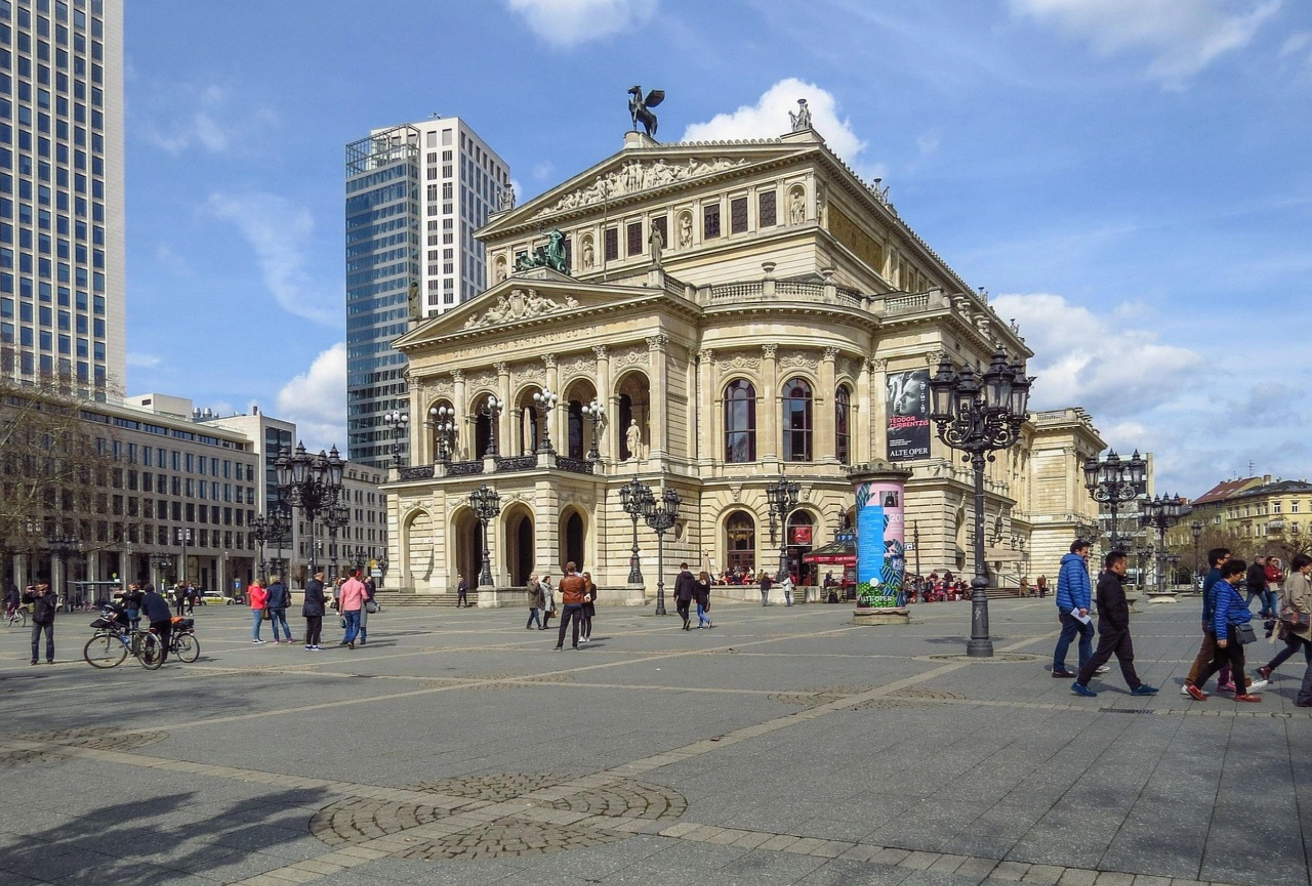 Historisches Opernhaus mit Säulen und Statuen, umgeben von modernen Hochhäusern, Menschen auf dem Platz davor
