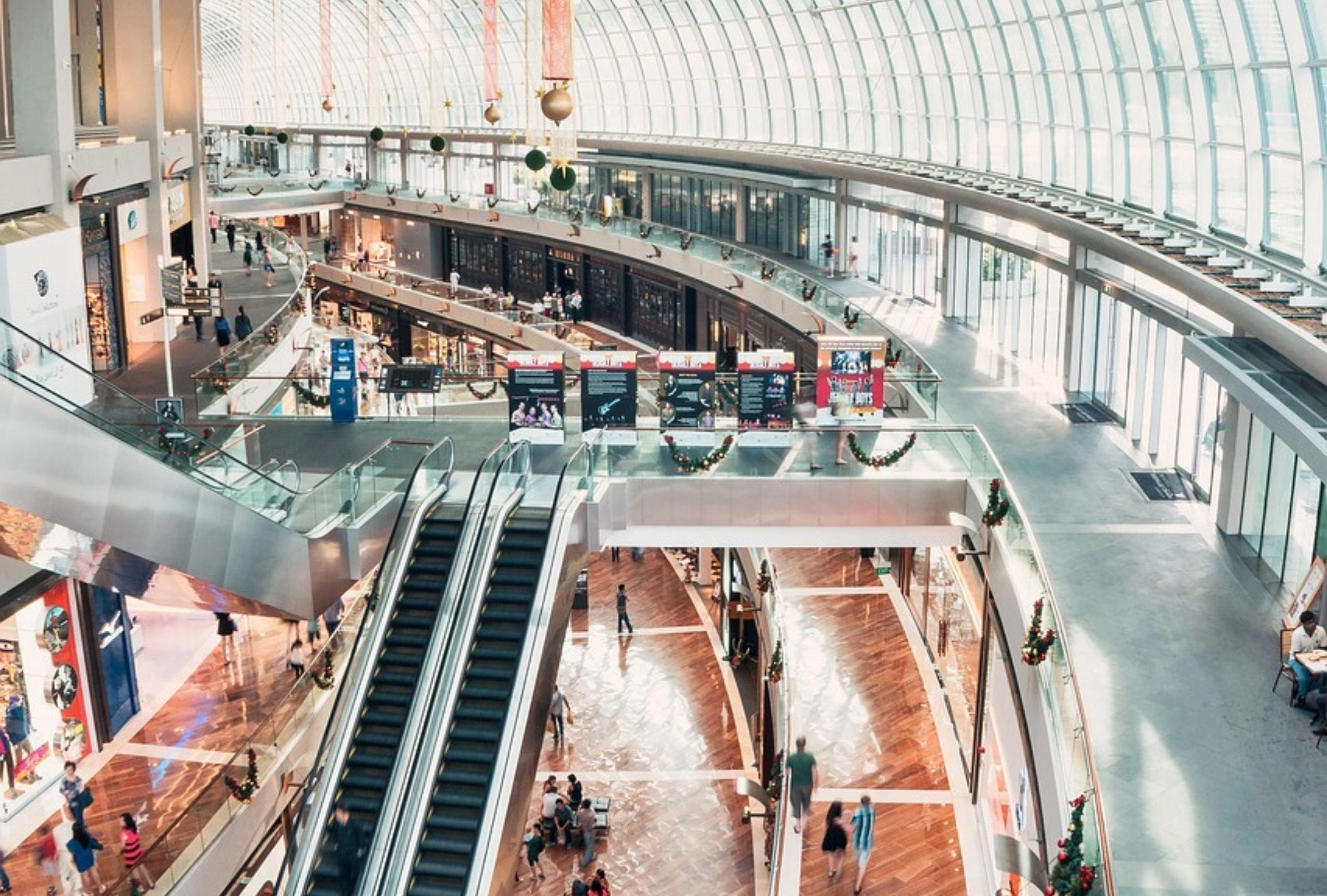 Innenansicht eines modernen Einkaufszentrums mit Rolltreppen, Glasdach und mehreren Besuchern
