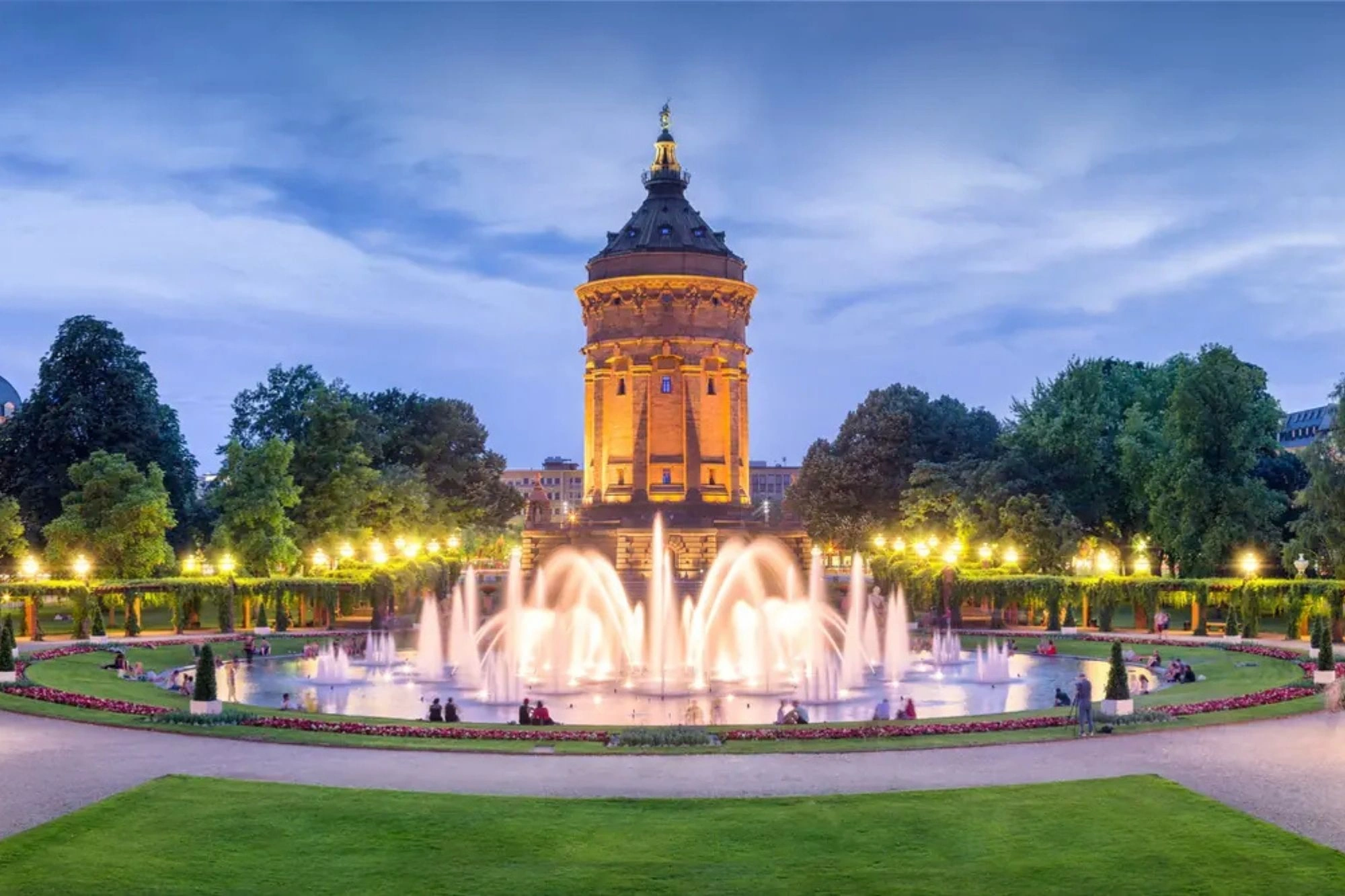 Stadtansicht mit dem Mannheimer Wasserturm im Hintergrund und grünen Parkanlagen.