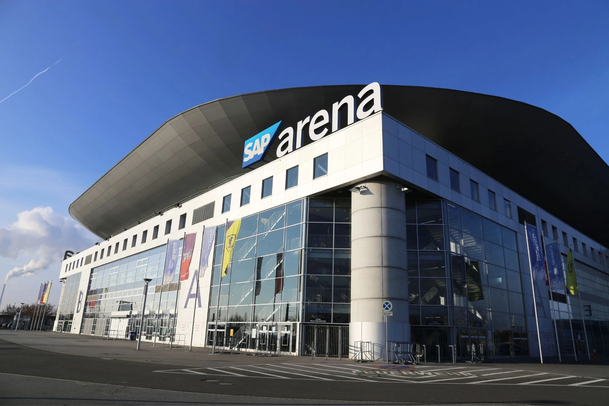 Außenansicht der SAP Arena mit Glasfassade und markantem geschwungenem Dach bei klarem Himmel