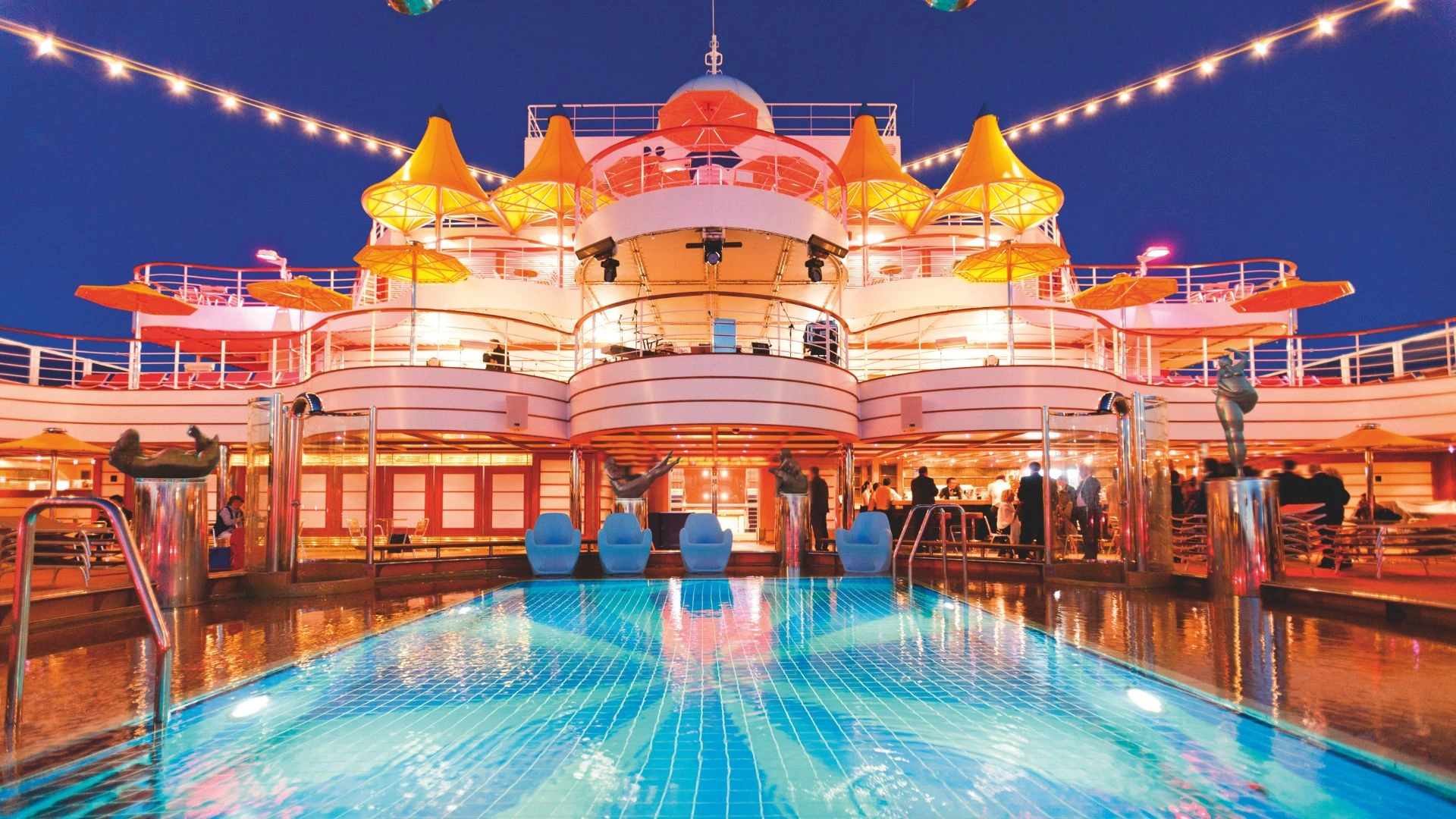 Schwimmbecken auf einem Kreuzfahrtschiff bei Nacht mit beleuchteten Sonnenschirmen.