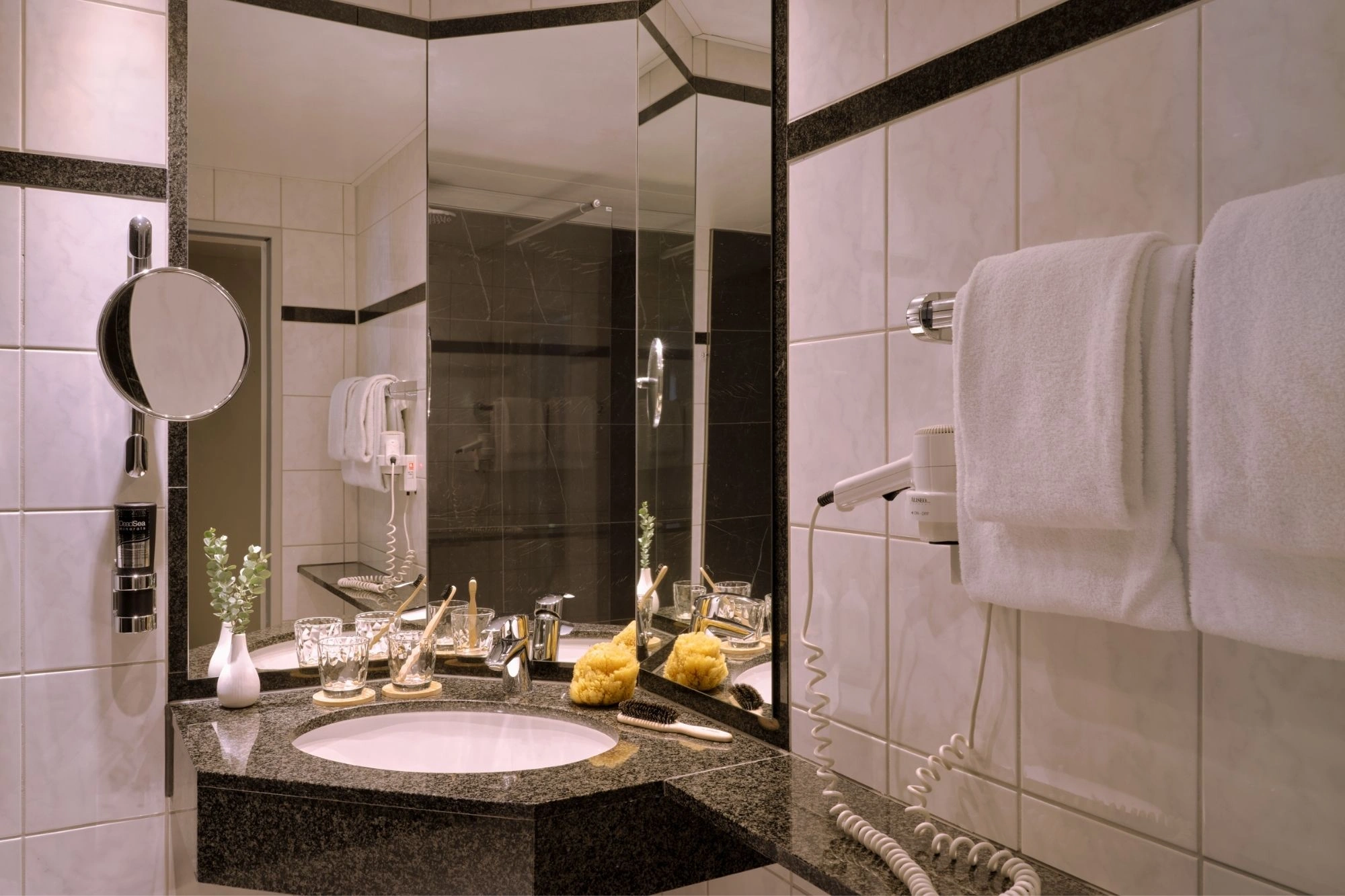 Badezimmer mit runder Waschbeckenplatte aus schwarzem Granit, zwei Handtüchern, einem Haartrockner, Spiegeln und Pflegeprodukten.