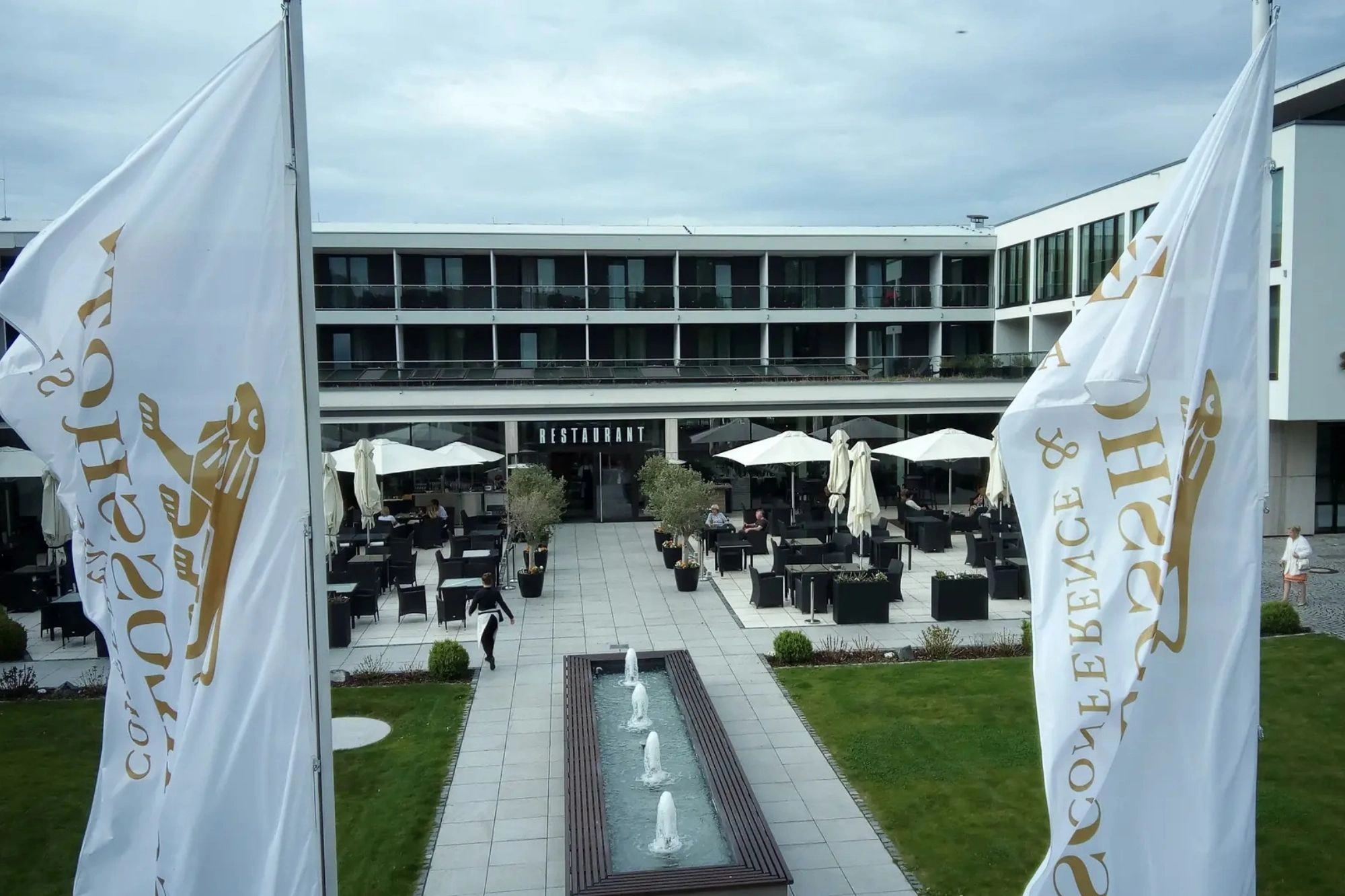 Blick auf die Terrasse des Restaurants im Schlosshotel Bad Wilhelmshöhe mit weißen wehenden Fahnen und goldenem Hotellogo