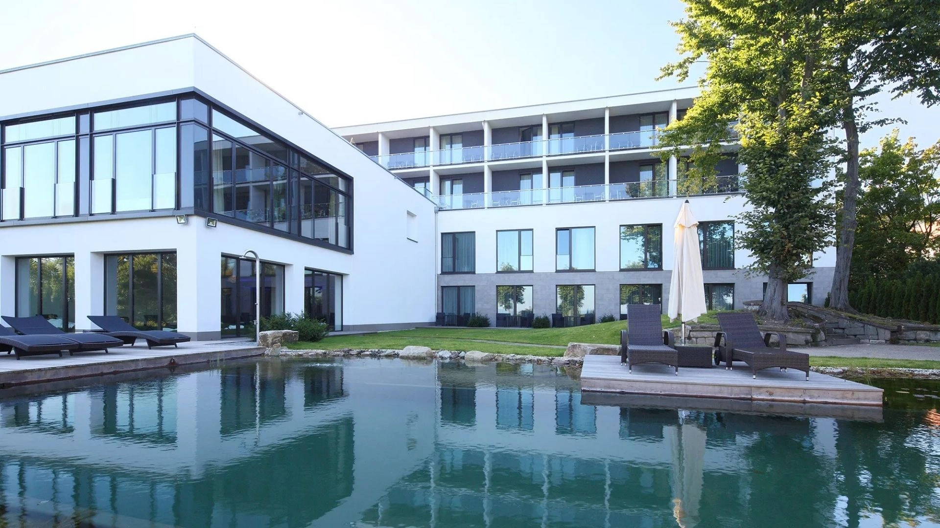 Schwimm- und Badeteich im Außenbereich des Schlosshotel Bad Wilhelmshöhe umgeben von einer Grünanlage, Liegen an der Rückseite des Hauses
