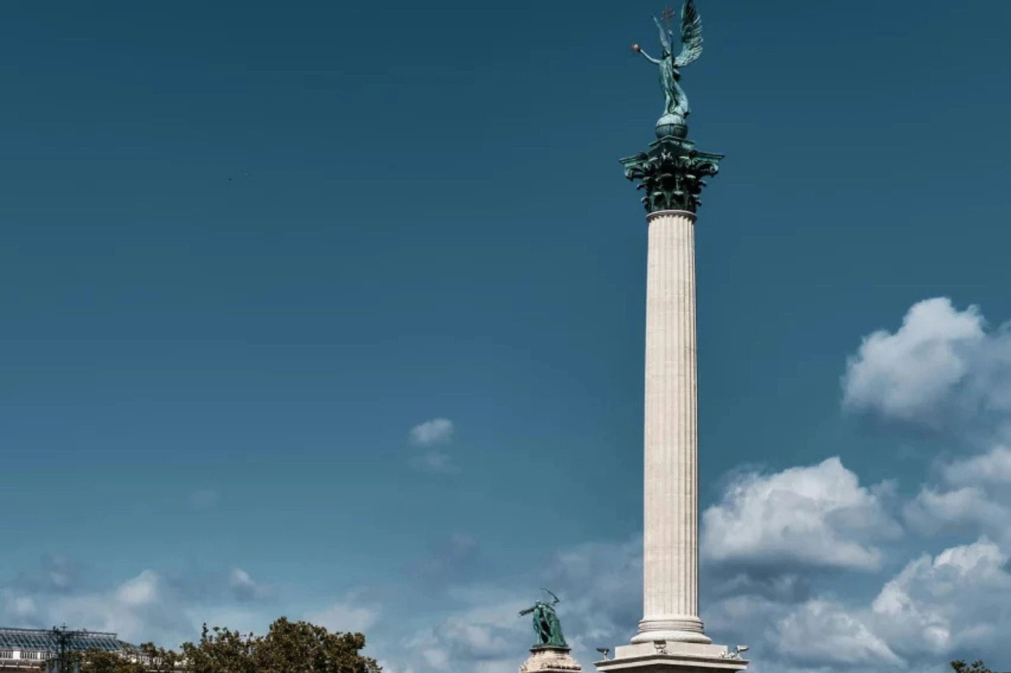 Städtereise Budapest zeigt das imposante Heldenplatz-Denkmal mit der hohen Säule, umgeben von Reiterstatuen und einer Kolonnade unter blauem Himmel.
