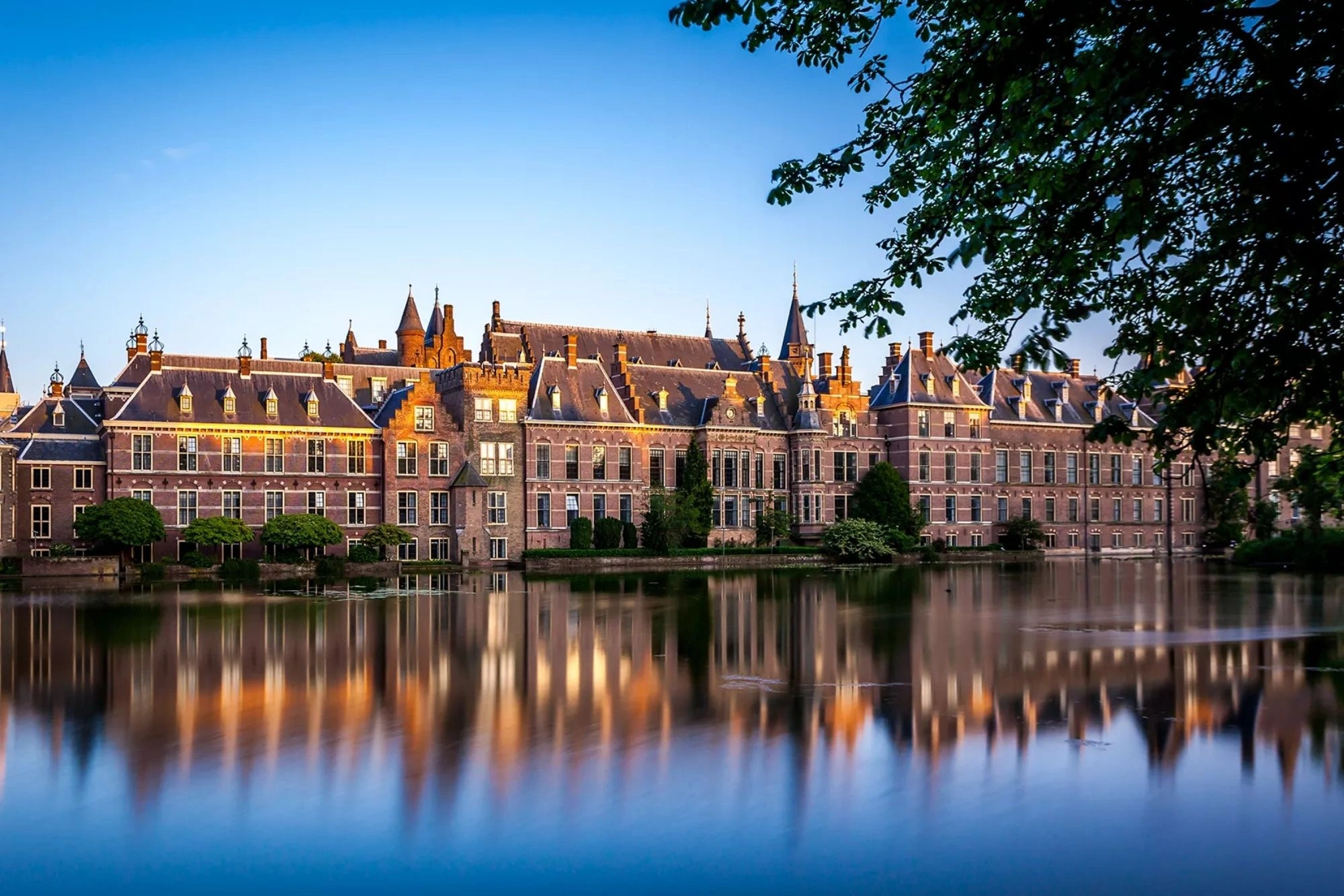 Ein Panorama des Binnenhofs in Den Haag, aufgenommen bei leichter Abenddämmerung. Sanfte Sonnenstrahlen reflektieren sich auf dem Wasser der Amstel und spiegeln die Architektur des historischen Gebäudes wider. Die ruhige Atmosphäre der Dämmerung verstärkt die Schönheit der Umgebung und lädt zur Besinnung ein.