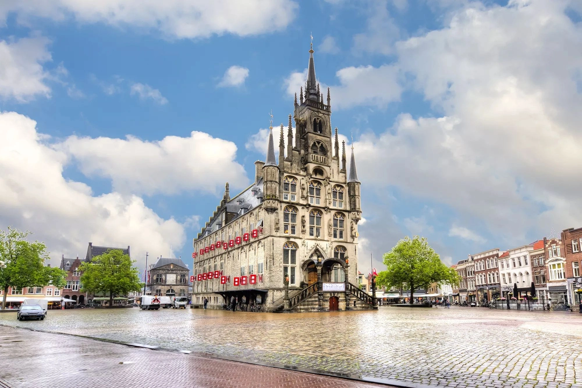 Das Rathaus am Marktplatz in Gouda, erfasst bei hellem Tageslicht. Die beeindruckende Fassade des historischen Gebäudes strahlt im Sonnenlicht, während der lebhafte Marktplatz mit seinen umgebenden Cafés und Geschäften eine einladende Atmosphäre schafft. Diese Szenerie verkörpert das charmante Flair der Stadt und lädt zum Verweilen ein.