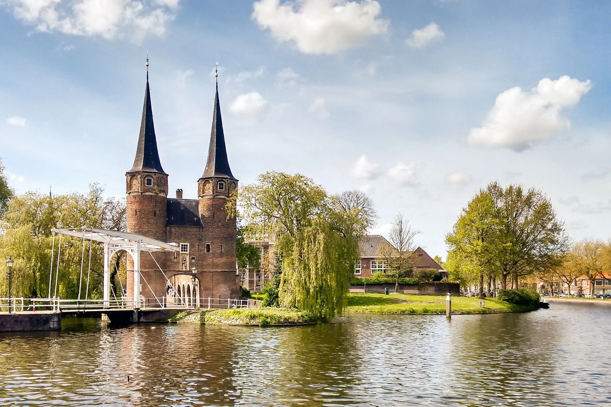 Das Oostpoort in Delft mit seinen zwei Türmen, umgeben von Wasser, grünen Wiesen und Bäumen, strahlt im Sonnenschein.