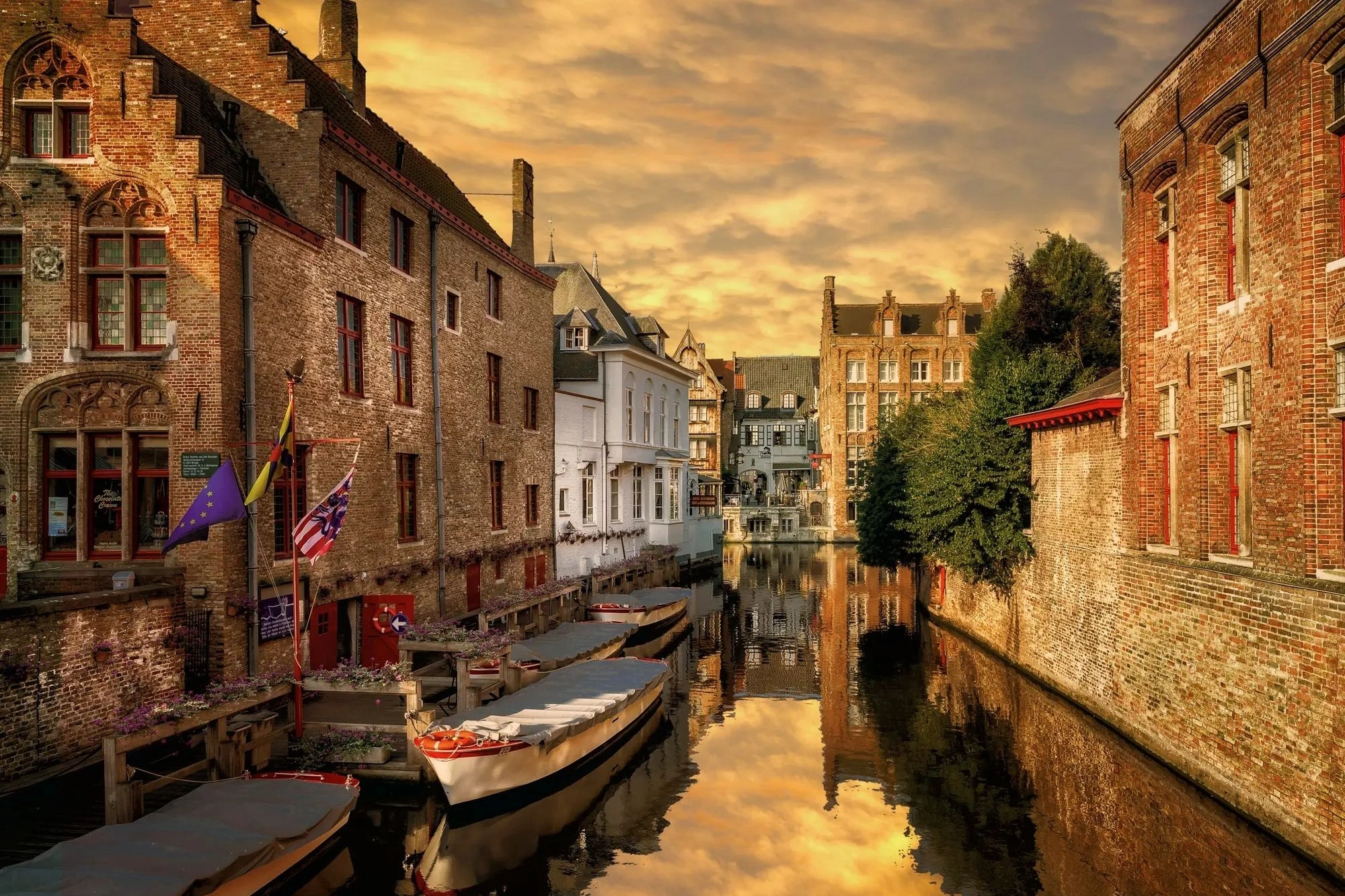 Boote, die auf einem ruhigen Kanal treiben, flankiert von Häusern auf beiden Seiten. Die Szene ist in warmes Licht der Abenddämmerung getaucht.