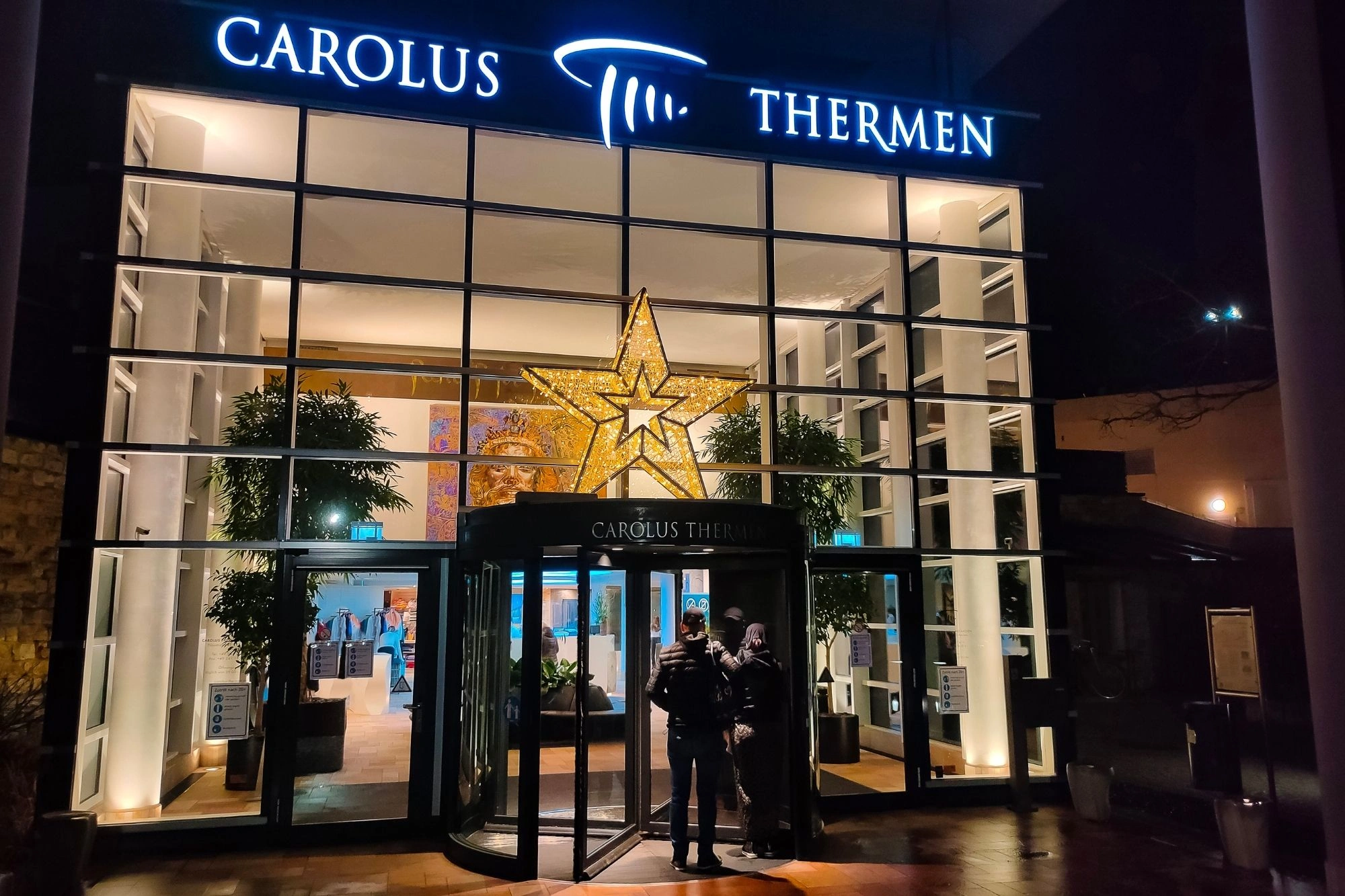 Eingang der Carolus Thermen mit beleuchtetem Schriftzug und großem Stern über dem Drehkreuz bei Nacht.