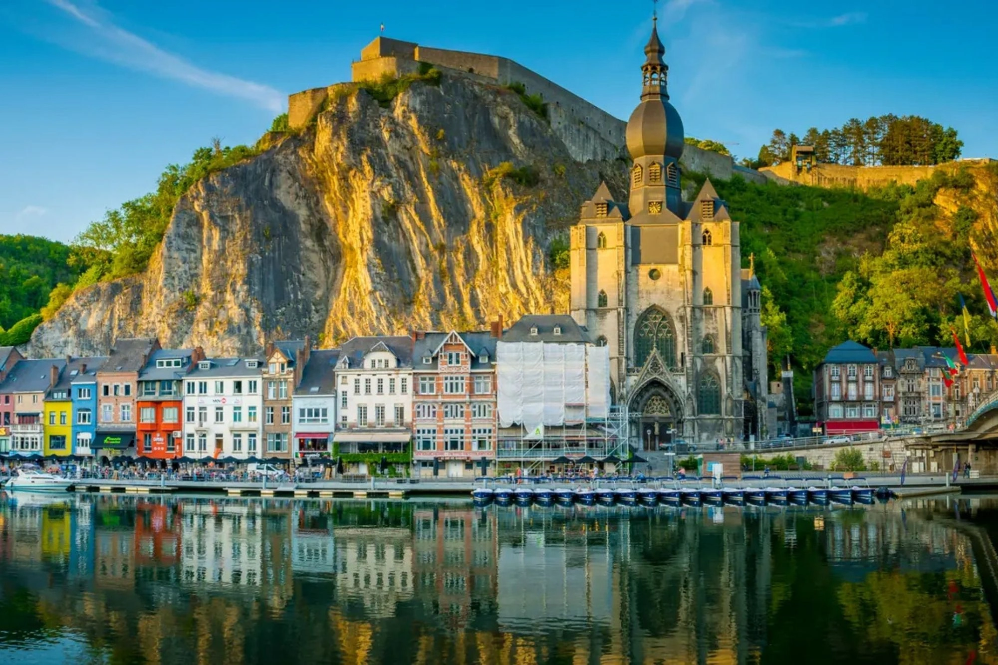 Blick vom Flussufer der Maas auf Dinant in den Ardennen bei sonnigem, klarem Himmel. Die Stadt, umrahmt von steilen Klippen, zeigt die jahrhundertealte Zitadelle, die majestätisch auf einem Felsen oberhalb thront.