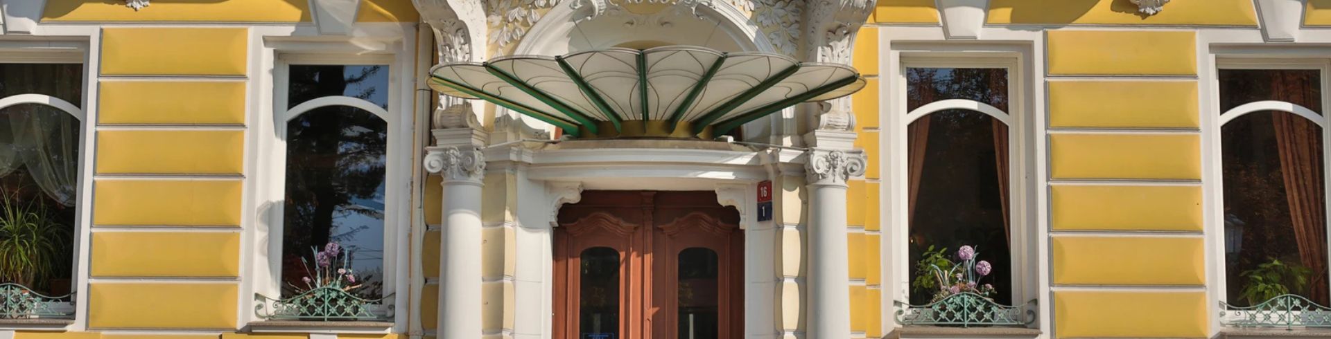 Eine gelbe Fassade mit dekorativem Balkon und Fenstern.