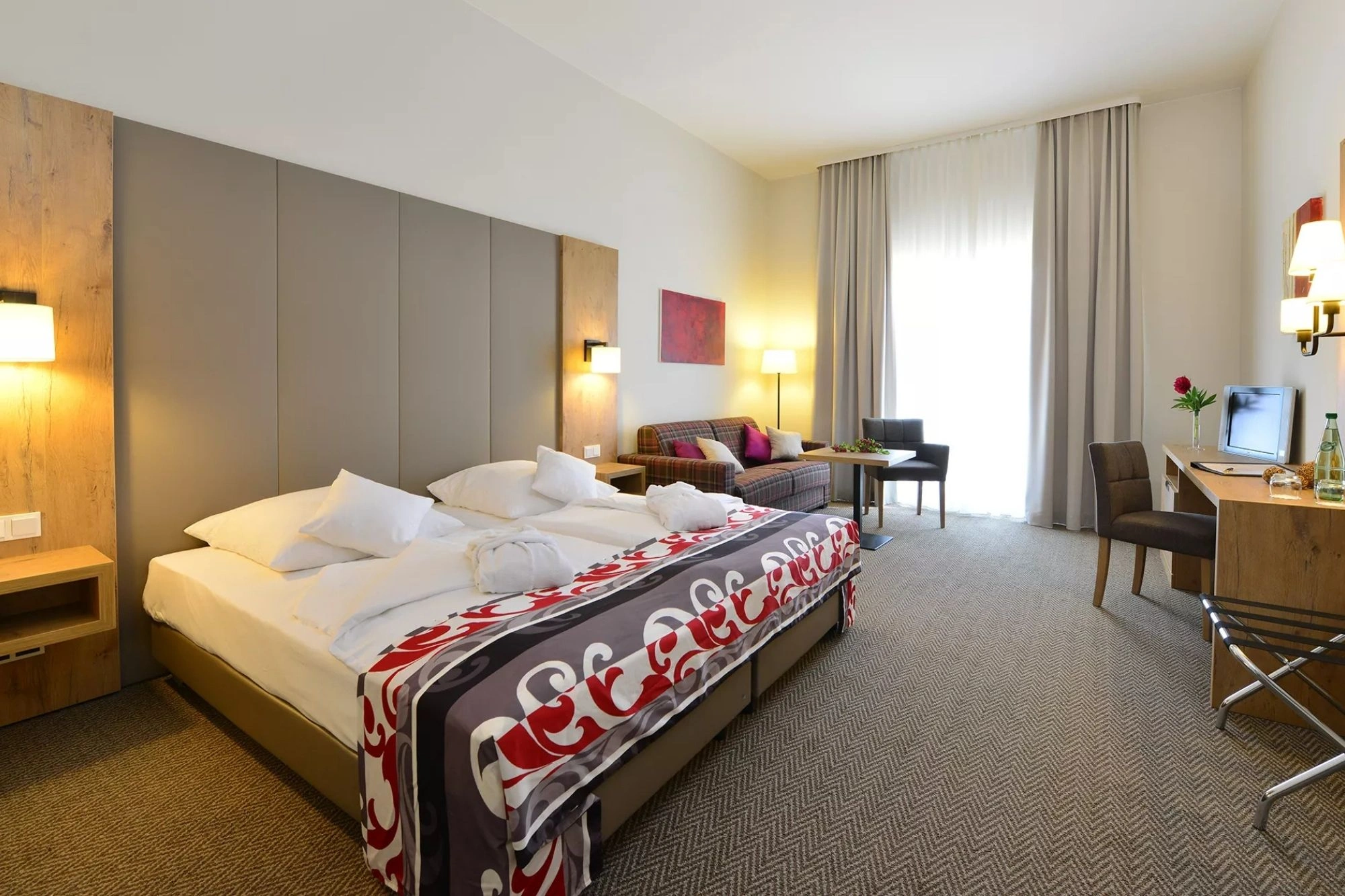 Blick in ein Zimmerbeispiel im Santé Royale Wolkenstein mit großen Doppelbett, Sitzbereich, Schreibtisch, Fernseher