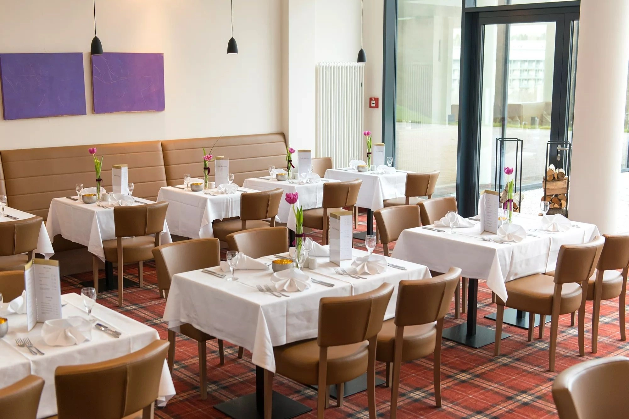 Das Restaurant im Santé Royale Wolkenstein ist in braunen und roten Naturtönen gehalten und mit verschieden großen eingedeckten Tischen dargestellt