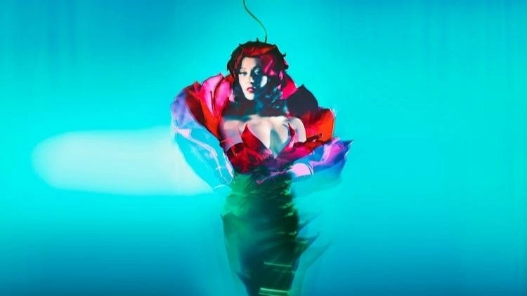 Person trägt ein rotes und pinkes Kleid mit voluminösen Ärmeln vor blauem Hintergrund