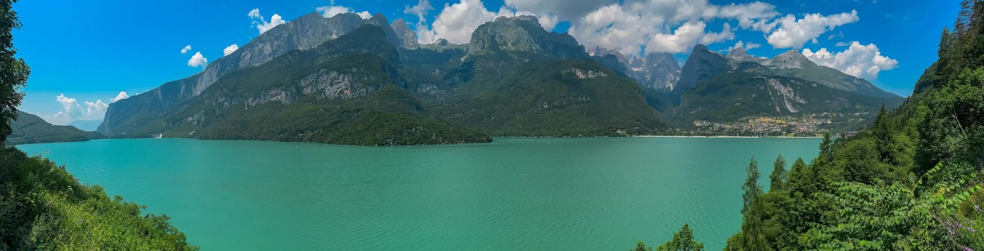 Greenery frames alpine retreat village at idyllic mountain lake Lago di Molveno with scenic view of majestic mountains Brenta Dolomites, National Park ... Mehr anzeigen