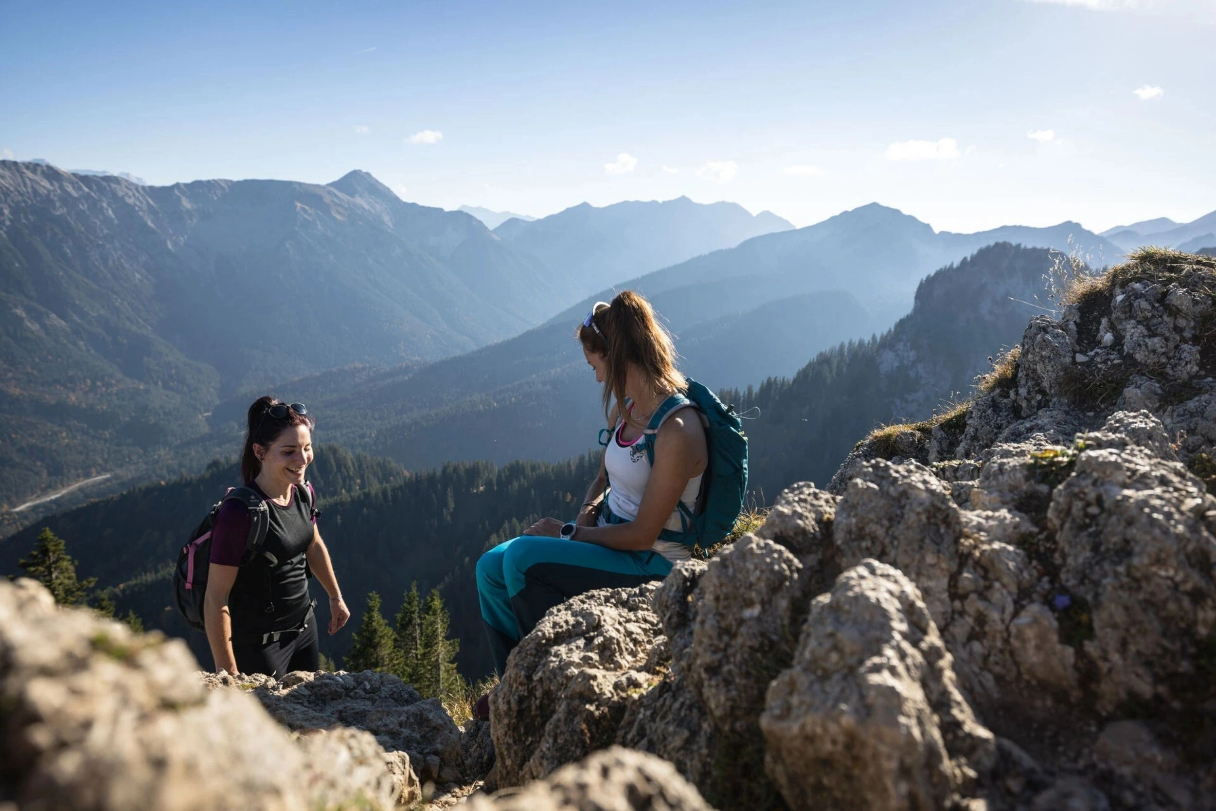Zwei junge Frauen beim Wandern machen Rast auf einem Felsen