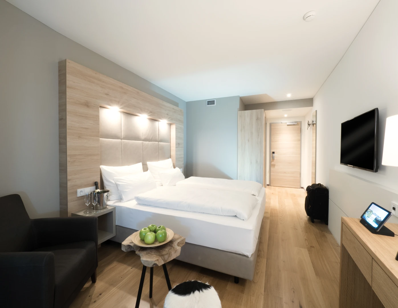 Modernes und stilvoll eingerichtetes Gästezimmer im Wonnemar Resort Wismar, ausgestattet mit einem komfortablen Doppelbett, eleganter Holzoptik und gemütlicher Sitzgelegenheit.