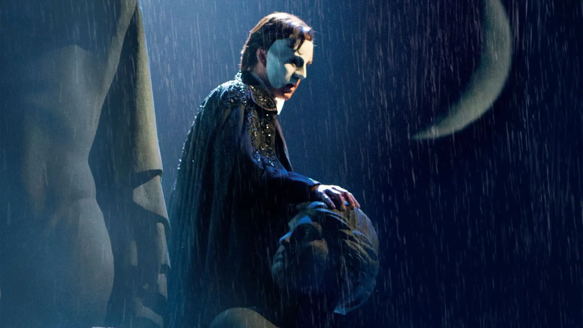 Schauspieler in Phantom der Oper Kostüm mit Maske und Umhang sitzt im Regen.
