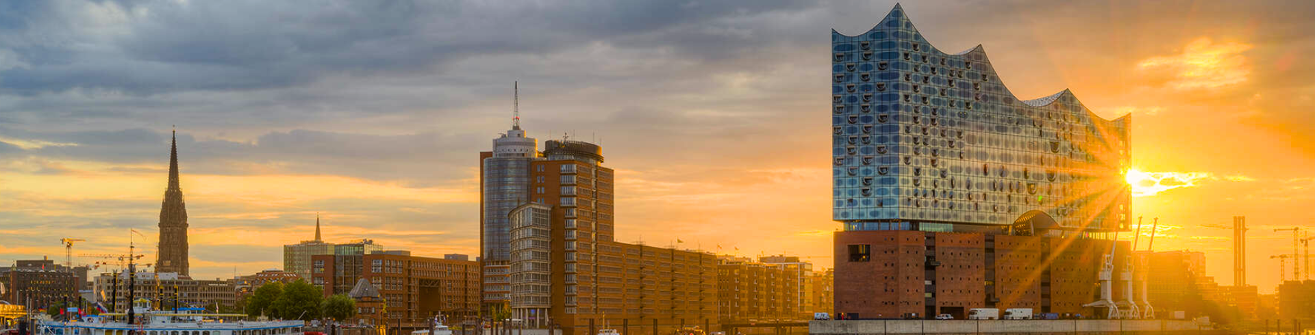 Hamburger Skyline mit Elbphilharmonie bei Sonnenuntergang und bewölktem Himmel