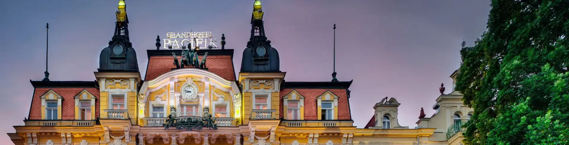 Oberer Teil des Grandhotels Pacifik mit verzierten Dachgiebeln, Türmen und beleuchteten goldfarbenen Figuren auf den Dachspitzen.