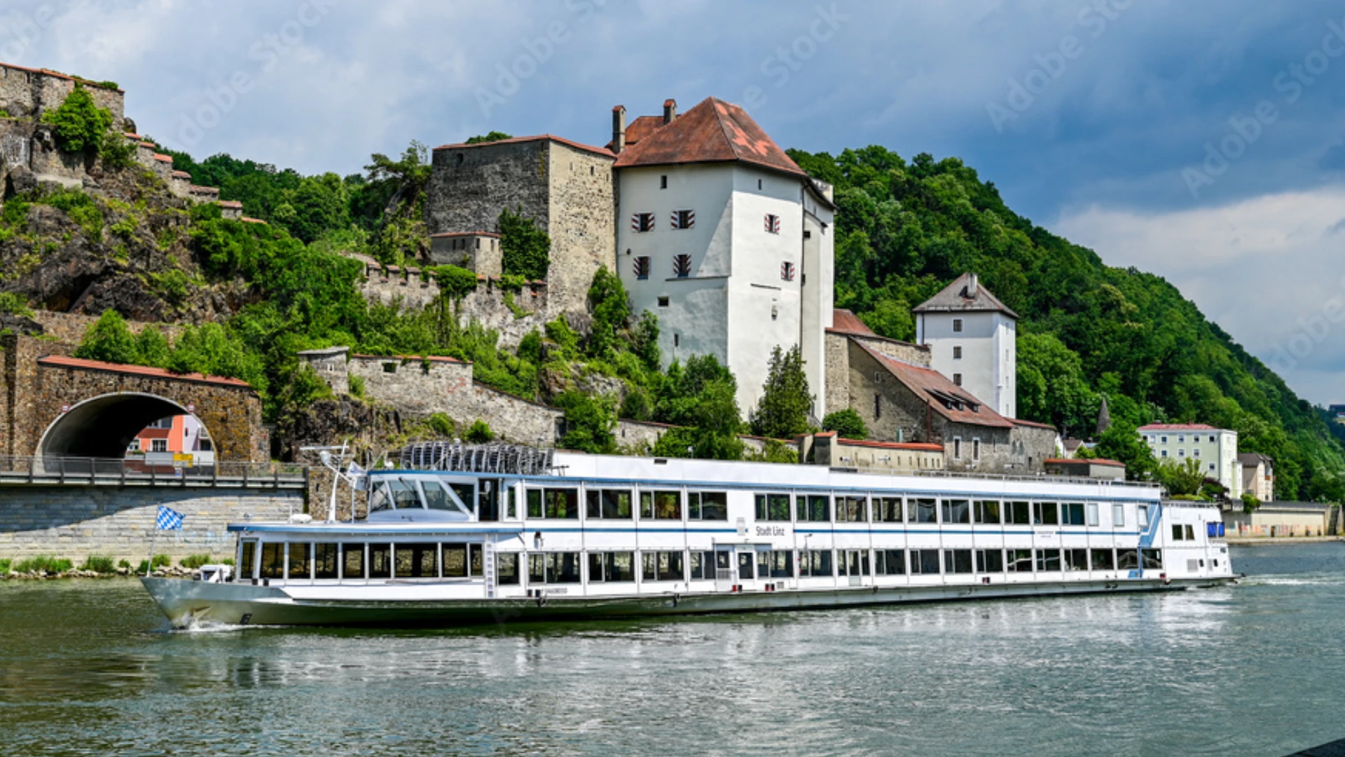 Weißes Passagierschiff auf Fluss vor historischer Burg mit runden Türmen und grünen bewaldeten Hügeln