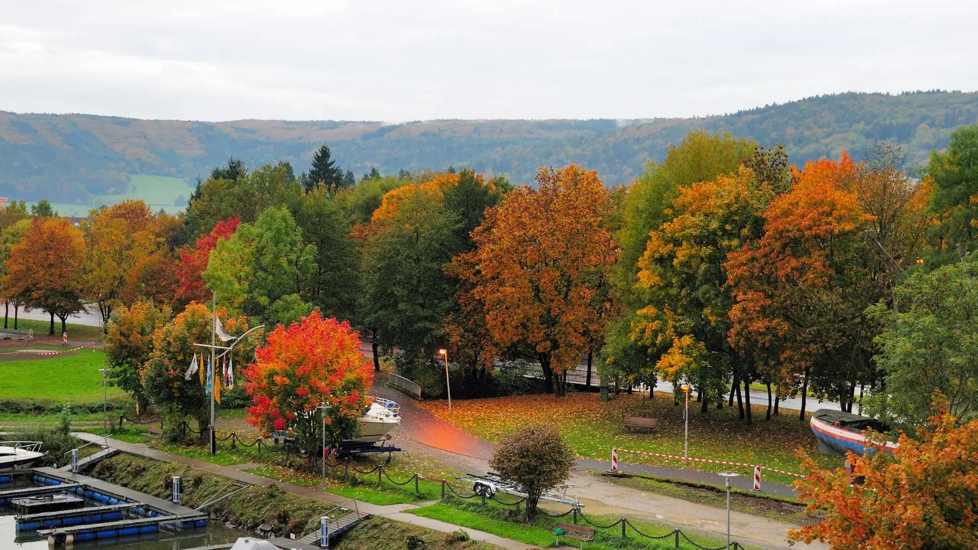 Herbstliche Bäume mit buntem Laub am Flussufer in Lohr am Main mit Booten und einem Weg entlang des Ufers