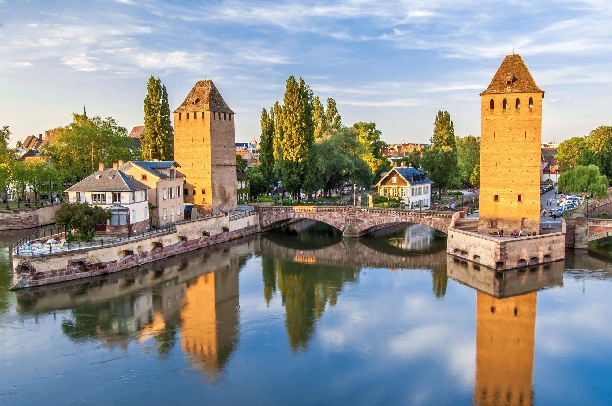 Panoramablick über den Fluss auf die Altstadt von Strasbourg, mit sanften sonnig-goldenen Farbtönen, die die Gebäude beleuchten.