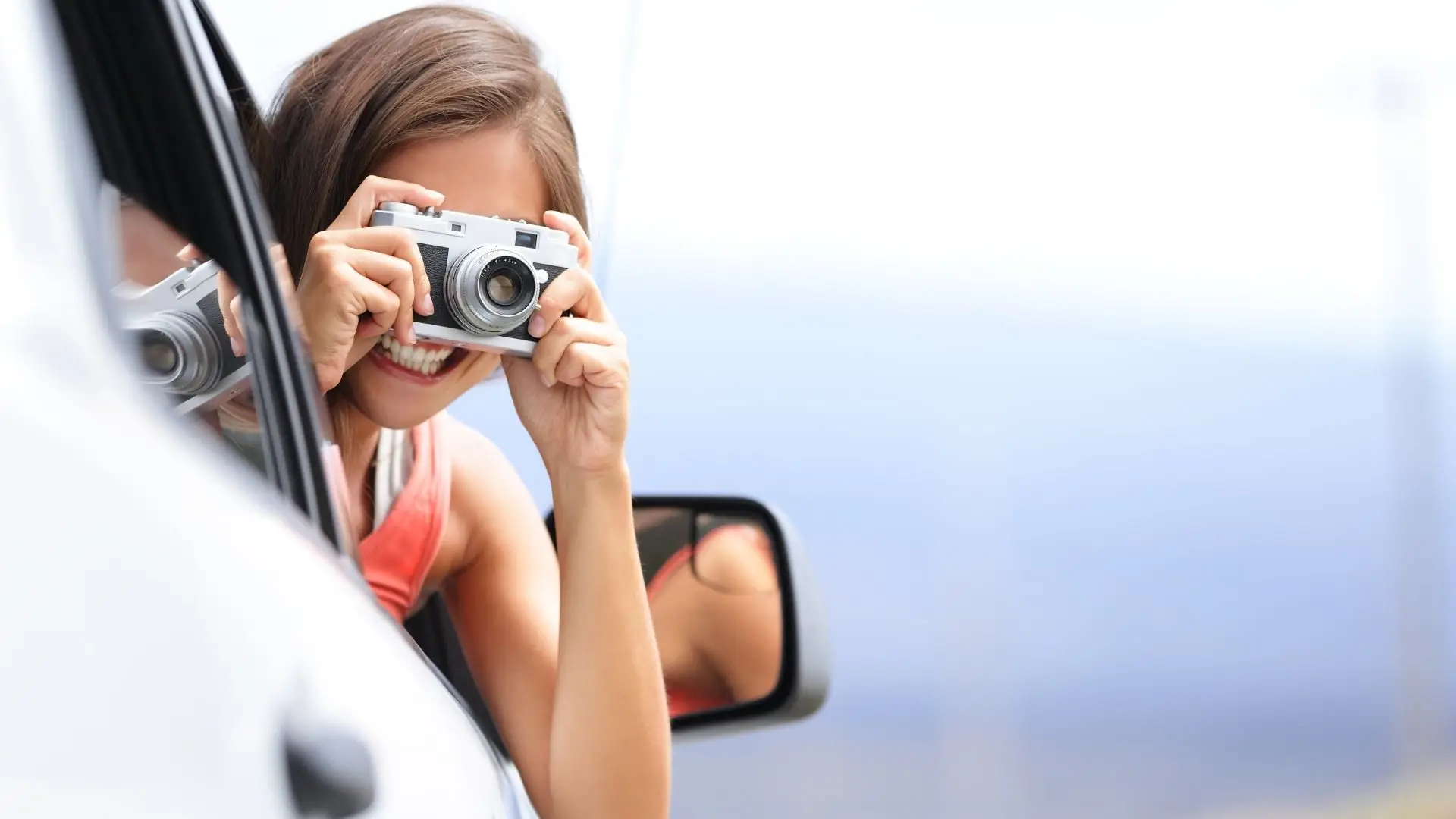 Frau lehnt aus dem Fenster eines weißen Autos und hält eine Kamera zum Fotografieren.