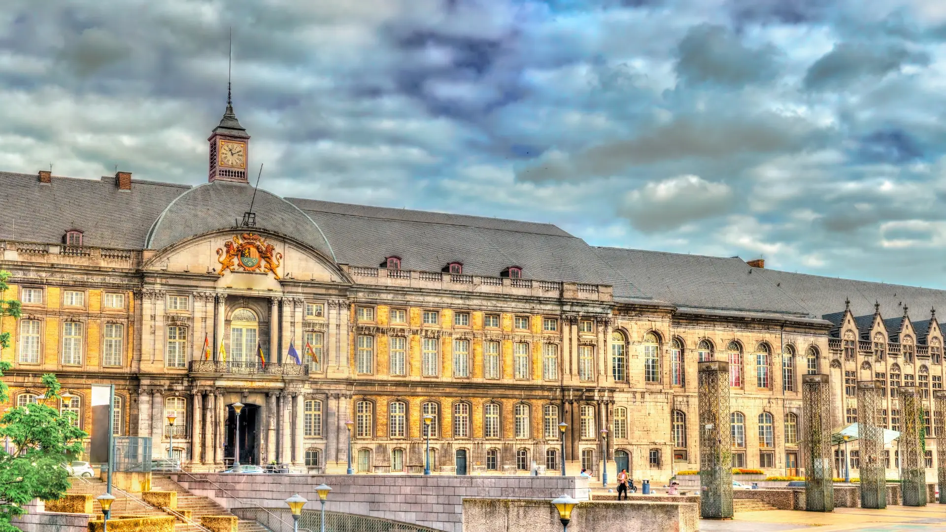 Palais des Princes-Évêques mit barocker Fassade, Uhrenturm und bewölktem Himmel im Hintergrund.